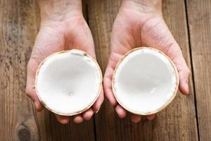 cut half coconut in hand and fresh coconuts on old wooden table for food. photo