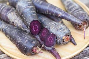 zanahoria morada en placa de madera, zanahoria fresca para cocinar vegetariano en mesa de madera. foto