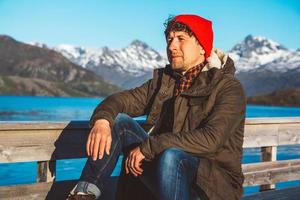 Traveler man sits in a boat near a wooden pier on a background of a mountain lake photo