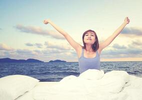 Tired sleepy woman waking up and yawning with a stretch while sitting in bed, sea view photo