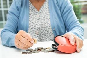 anciana asiática mayor o anciana sosteniendo contando dinero de moneda en el bolso. pobreza, problema de ahorro en la jubilación. foto