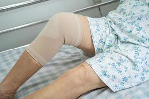 Asian senior or elderly old lady woman patient with knee support pain joint on bed in nursing hospital ward, healthy strong medical concept. photo