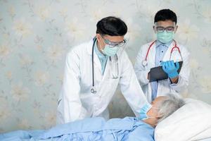 Asian doctor team check old senior lady patient for disease to motivation new normal to treat infection Covid-19 Coronavirus at hospital ward. photo