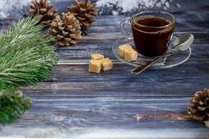 una taza de café aromático con azúcar morena, adornos navideños, ramas de un árbol de navidad. concepto de vacaciones año nuevo. sobre un fondo de madera. foto