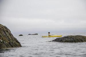 Woman kayaking in a yellow kayak around rocks in the ocean photo