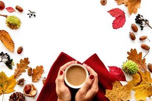 Autumn frame made of dried leaves, pine cones, berries, acorns, warm scarf and hand with cup of coffee on white background. Template mockup fall, halloween. Flat lay, copy space background photo