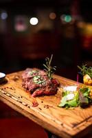 entrecot de ternera bistec de carne a la parrilla en tabla de cortar de madera con rama de romero, pimienta y sal. foto