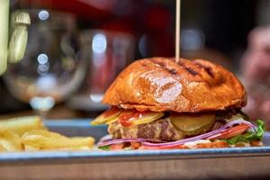 Sabrosa hamburguesa a la parrilla con carne, queso, tocino y salsa en la mesa de madera con papas fritas y cerveza foto