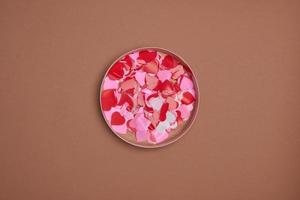 composición del día de San Valentín. caja de regalo, confeti, postal de sobre con corazón rojo sobre fondo pastel foto