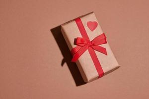 composición del día de San Valentín. Caja de regalo o presente envuelta en papel artesanal con corazón sobre fondo pastel foto