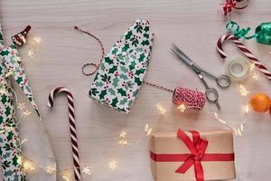 Christmas composition. Giftboxes, presents wrapping with paper and ribbon, lights, candy canes on wooden background. Holdiay DIY handmade home decoration. Winter, new year Flat lay, top view photo