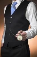 man in elegant suit on orange background holding a pocket watch hanging from his waistcoat photo