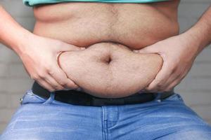 La mano del hombre sujetando el exceso de grasa abdominal, concepto de sobrepeso foto