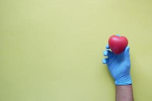 man hand in protective gloves holding red heart photo