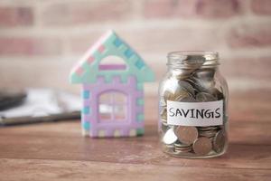 Concepto de finanzas de la casa con modelo de casa y tarro de monedas de ahorro en la mesa