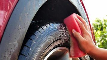 travailleur lave les roues de la voiture avec une éponge sur un lave-auto. bannière d'entreprise de lavage de voiture. video