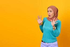 Shocked young Asian woman raised hand with copy space on yellow background