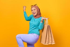 Excited and cheerful young Asian woman holding shopping bags on yellow background photo