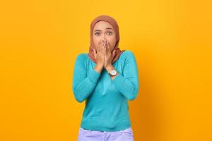 Shocked young Asian woman covering mouth with hand on yellow background