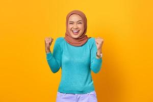 Cheerful young Asian woman celebrating victory, euphoric over achievement on yellow background photo