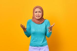 Confused young Asian woman shrugging raise hands on yellow background photo