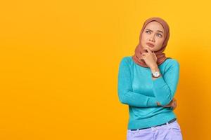 Pensive young Asian woman thinking about something on yellow background photo