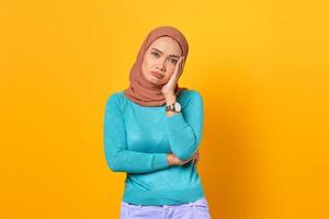 Frustrated young Asian woman holding face with a hand on yellow background photo