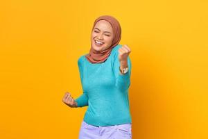 Cheerful young Asian woman celebrating victory, euphoric over achievement on yellow background photo