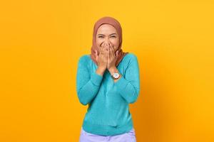 Happy young Asian woman covering mouth with both hands on yellow background