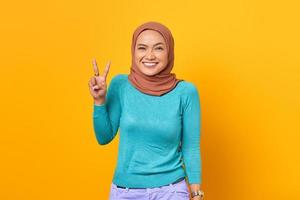 Beautiful cheerful young Asian woman showing peace sign on yellow background photo