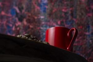 Taza de café rojo sobre la mesa de madera, granos de café, fondo abstracto