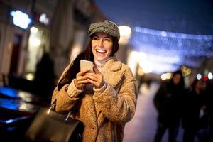 Pretty young woman using her mobile phone in the street at Christmas time photo