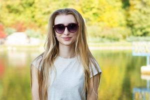 primer plano de la hermosa joven con gafas de sol, contra el verde del agua del parque de verano. foto