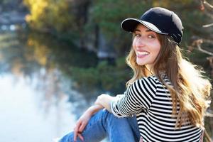 Hermosa sonrisa hipster girl en una gorra negra sobre un fondo de bosque otoñal foto