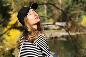 Close up Girl enjoys a sunny day with closed eyes sitting against background of a career and trees photo