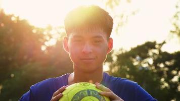sorridente menino adolescente no sportswear segurando uma bola de futebol no campo de futebol. jogador de futebol treinando no campo de futebol. video