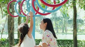 Mother helps her little daughter to hang on colorful monkey bars in the playground. Play is learning in childhood. video