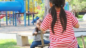 actieve zusjes spelen op een wip in de buitenspeeltuin. gelukkig kind meisjes glimlachen en lachen op kinderspeelplaats. spelen is leren in de kindertijd. video
