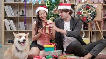 Sorprenda al equipo de dos compañeros de trabajo y al perro cerca dando regalos mientras habla de negocios antes de las vacaciones de la empresa en el lugar de trabajo de la oficina, está decorado para la celebración del festival de Navidad y la fiesta de año nuevo. video