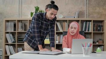 due giovani colleghi di startup che sono persone islamiche parlano di successo lavorando in un'attività di e-commerce con un sorriso. utilizzare il laptop per la comunicazione online via Internet in un piccolo ufficio. video