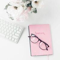 white workspace with light pink note book and white flower with coffee on white table. photo