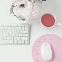 white workspace with light pink note book and white flower with coffee on white table. photo