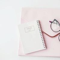 white workspace with light pink note book and white flower with coffee on white table. photo