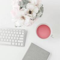 white workspace with light pink note book and white flower with coffee on white table. photo