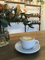 Coffee milk with a heart shape in a cup with a cafe and plant background photo