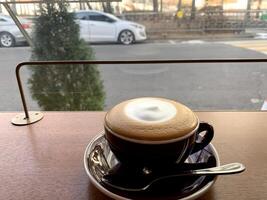 Café con leche con crema en el medio en una taza blanca con un fondo de calle foto