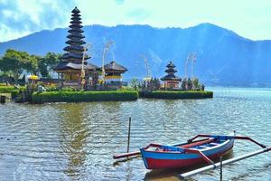 lake with a temple and a boat and a hillside photo