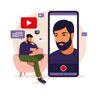 Man video blogger sitting on sofa with phone and recording video with smartphone. Different social media icons. Vector illustration in flat style.