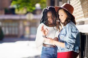 dos amigos mirando su teléfono inteligente juntos. mujeres multiétnicas. foto