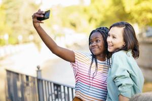 dos amigas multiétnicas haciendo selfie al aire libre.
